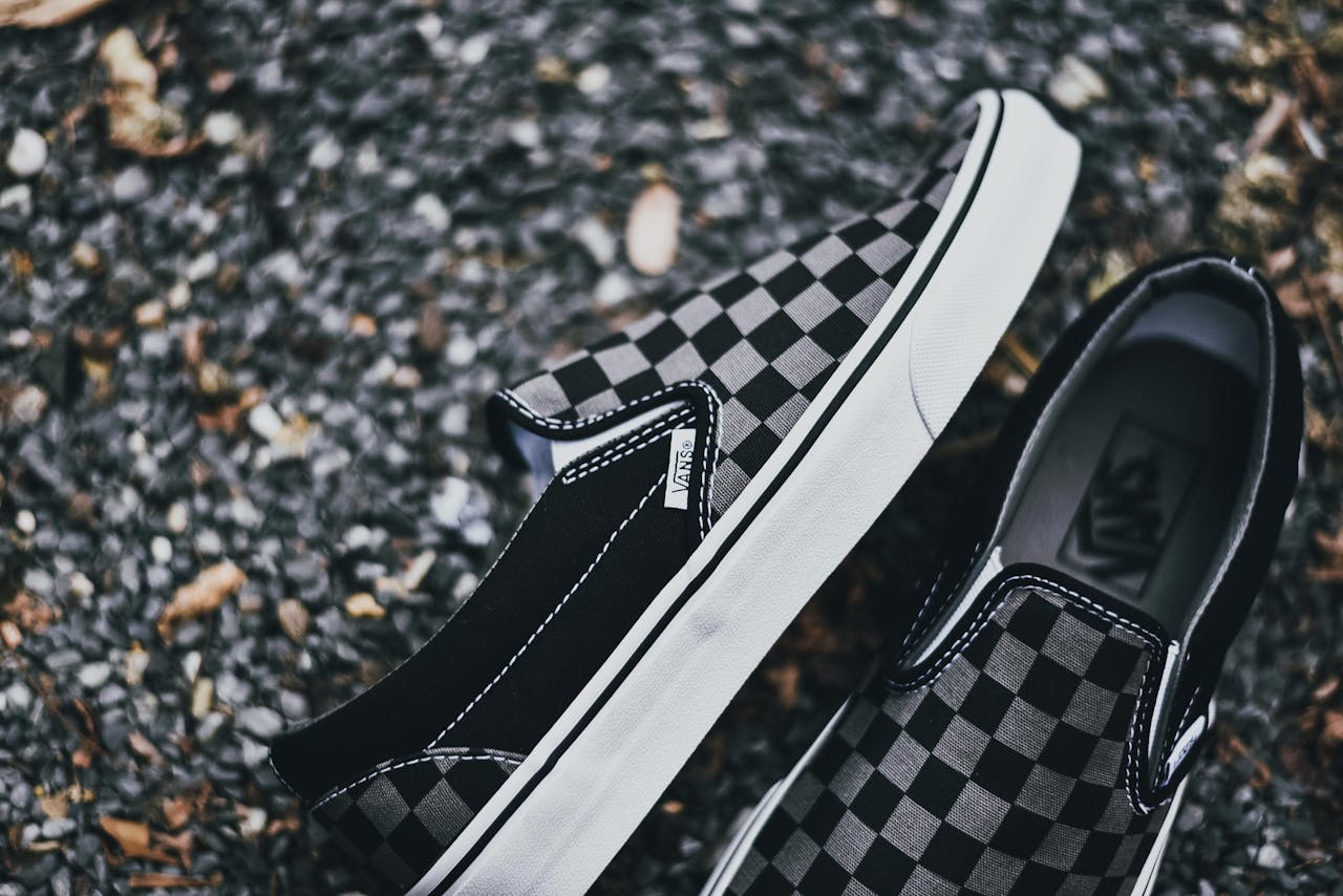 Close-up of black and white checkered slip-on sneakers on gravel surface showcasing textured design.