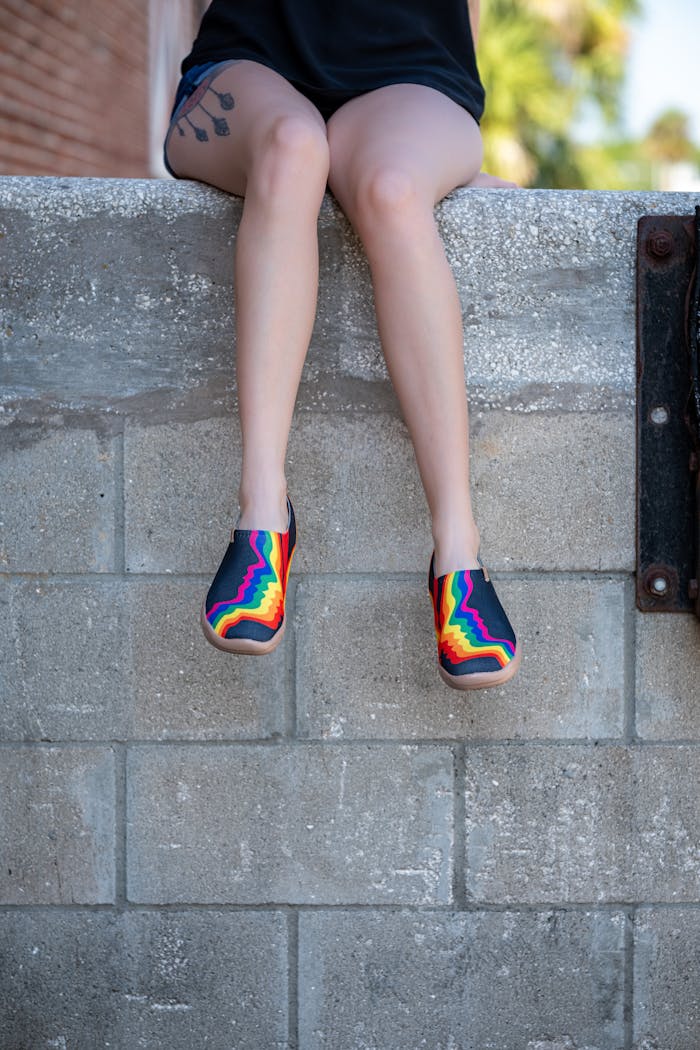 Young person in colorful sneakers sitting on an urban concrete wall. Casual fashion.