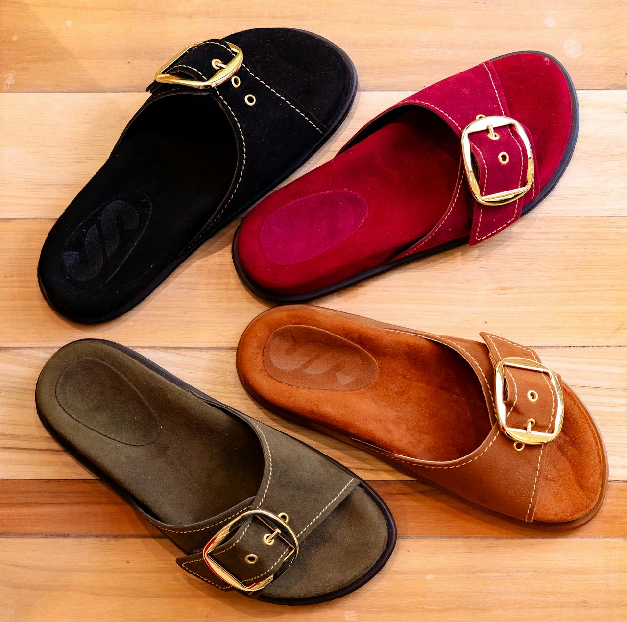 A variety of stylish leather buckle sandals arranged on a wooden floor.