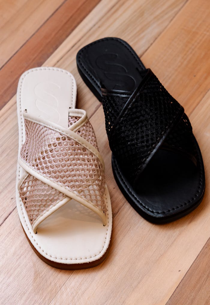 Elegant mesh sandals in beige and black placed on a wooden floor, showcasing modern footwear design.